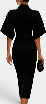 Back view of a woman wearing a Mahaute black midi dress with flared sleeves, cinched waist, and a back slit.