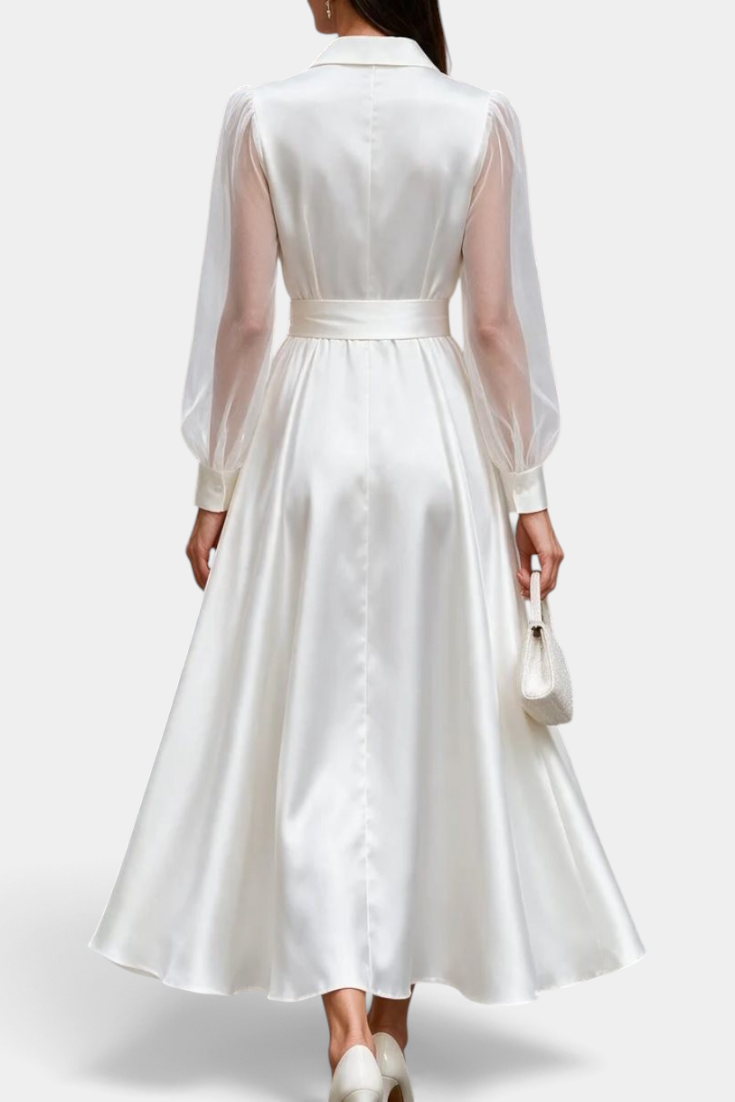 Back view of a Mahaute satin midi shirt dress in white with sheer long sleeves and a tied waist, worn with heels.