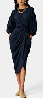 Robe mi-longue Mahaute Merjem avec taille nouée, drapée et manches ballon, portée sur un fond neutre.