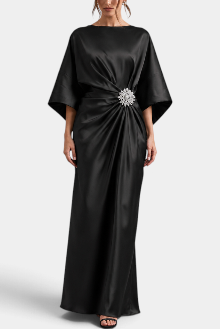 Mahaute Ubélia long black satin evening gown with cape sleeves, asymmetric waist drape, and a sparkling jewel brooch.