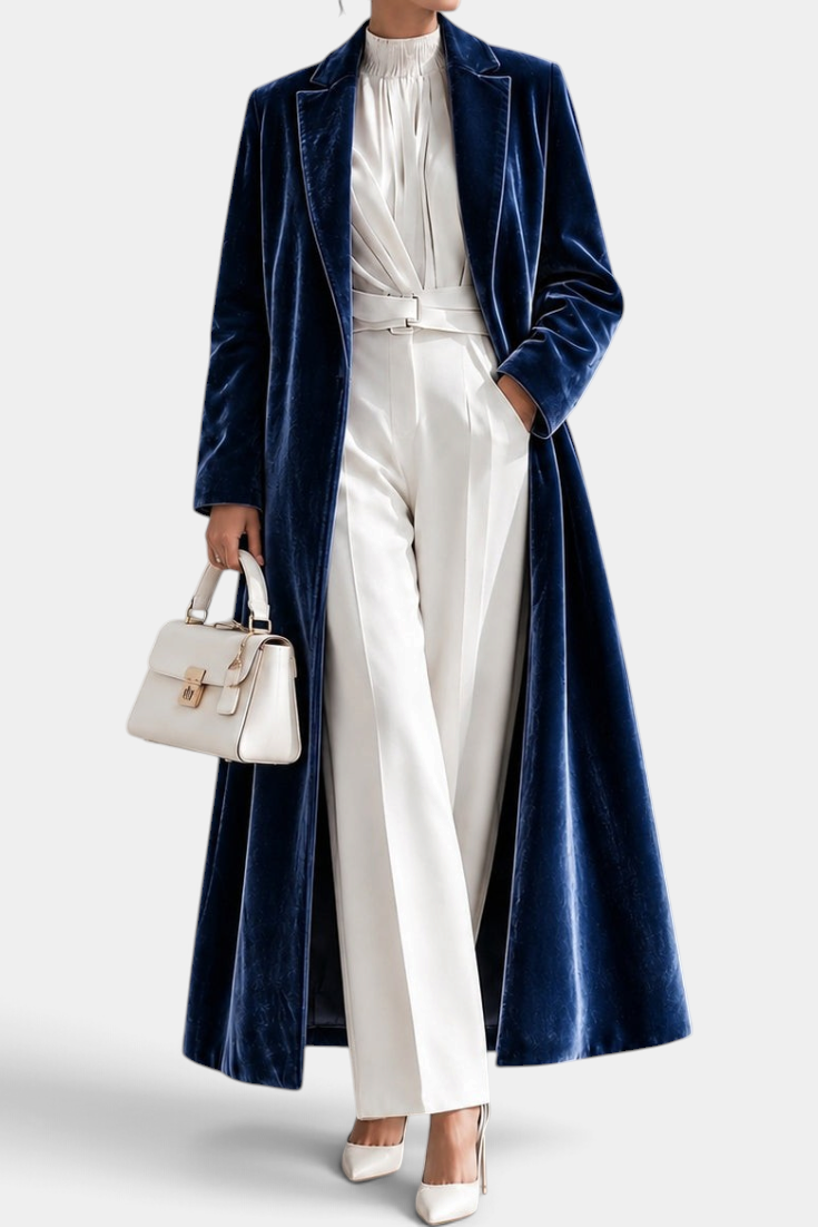 Mahaute long blue velvet coat with elegant lapels, worn over a white outfit with a matching handbag.