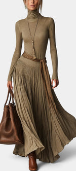 Robe longue Mahaute Zélidie avec col roulé, jupe plissée et taille nouée, portée avec un style élégant et sophistiqué.