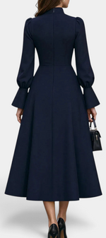 Mahaute Albena navy midi dress with a high ruffled collar, cinched waist, and voluminous puff sleeves, back view.
