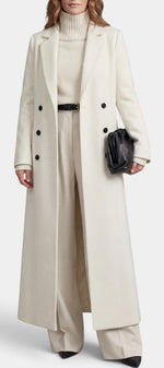 Manteau long Amalberge Mahaute couleur crème avec double boutonnage et col tailleur, porté en extérieur.