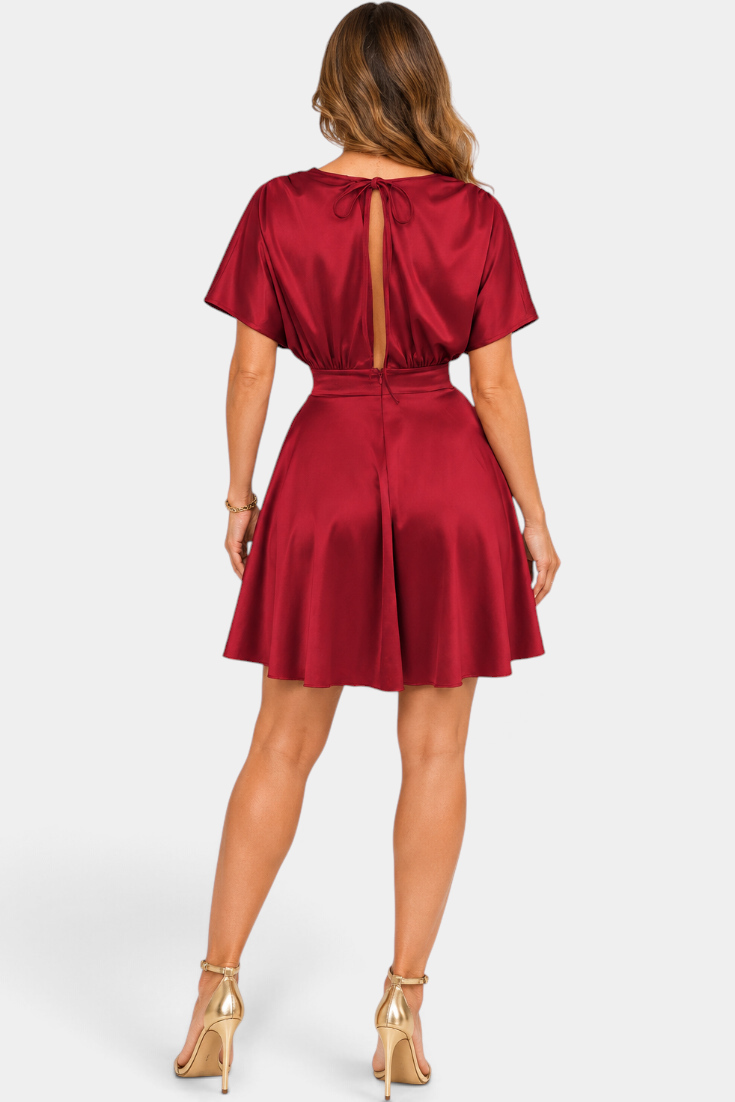 Mahaute Ambre short red satin dress with open back, tie detail, and flared skirt, worn with gold high heels.