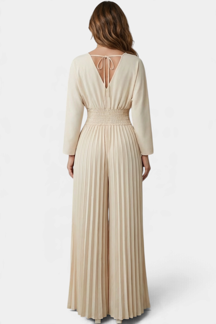 Mahaute beige pleated wide-leg jumpsuit with a V-neck back and tie detail, worn by a woman from behind.