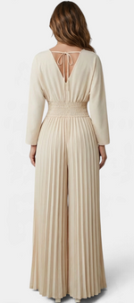 Mahaute beige pleated wide-leg jumpsuit with a V-neck back and tie detail, worn by a woman from behind.