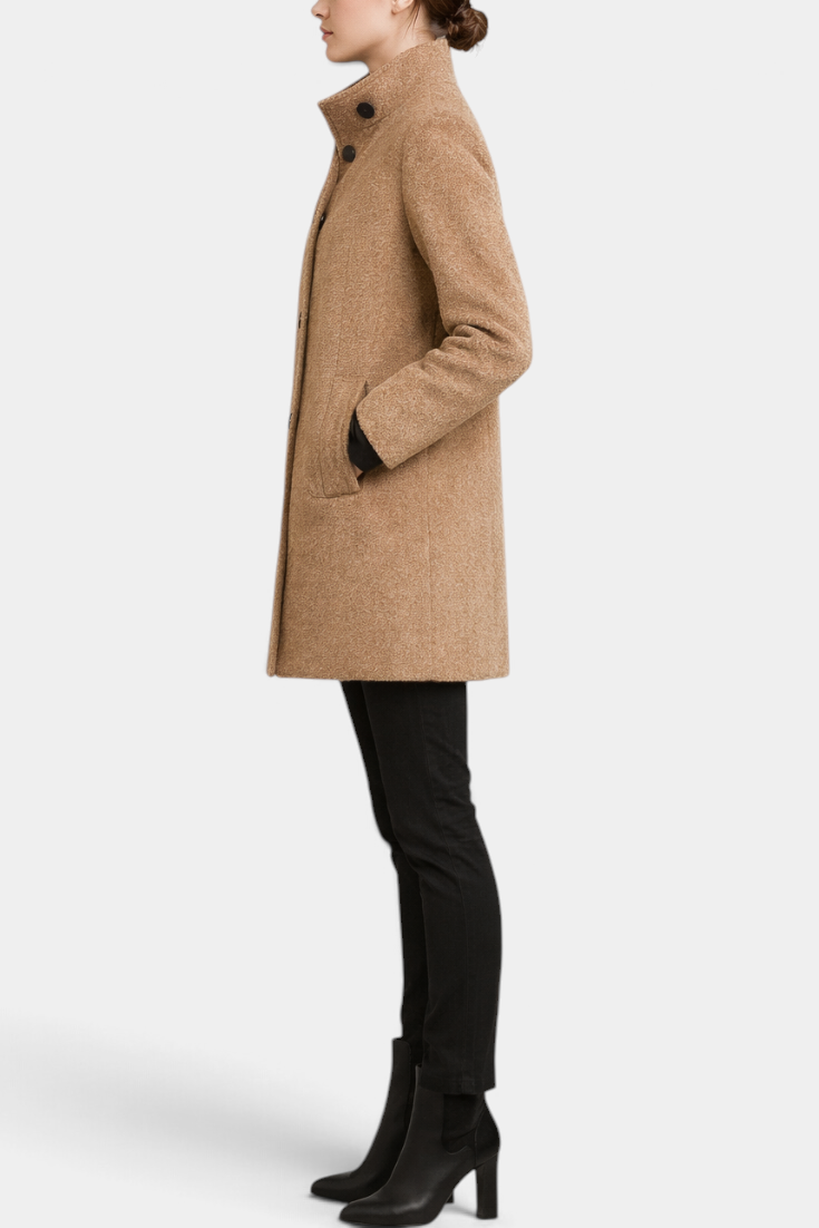 Mahaute Bellarya tan mid-length coat with a high collar, button front, and patch pockets worn by a model in profile.