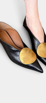 Mahaute Billini black pointed-toe pumps with a low heel and a large circular gold metallic ornament on the front.