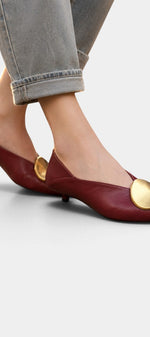 Mahaute Billini burgundy pointed-toe kitten heels with a large gold metallic ornament worn with cropped jeans