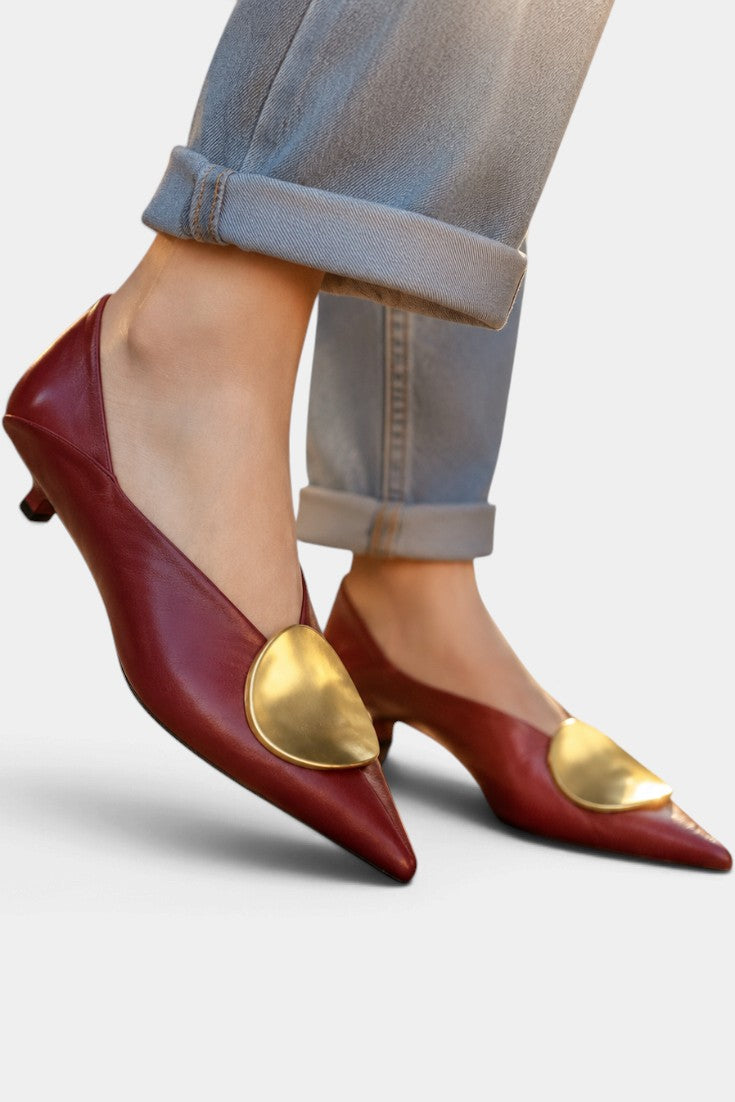 Mahaute Billini burgundy pointed-toe kitten heels with a large gold metallic ornament worn with cuffed blue jeans