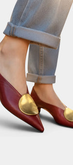 Mahaute Billini burgundy pointed-toe kitten heels with a large gold metallic ornament worn with cuffed blue jeans