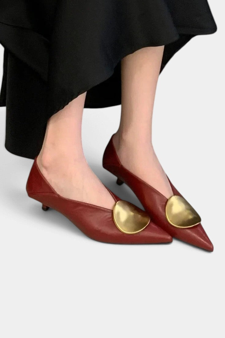 Mahaute Billini pointed-toe kitten heel pumps in deep red leather with a large gold metallic ornament on the front.