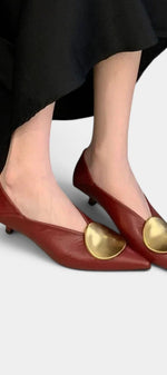 Mahaute Billini pointed-toe kitten heel pumps in deep red leather with a large gold metallic ornament on the front.