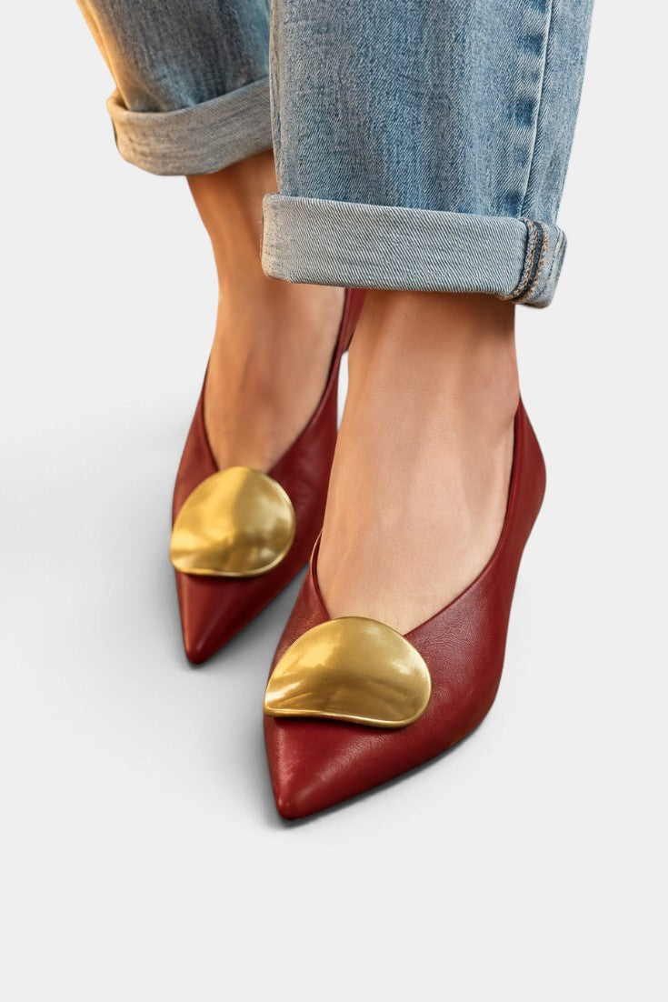Mahaute Billini red pointed-toe pumps with a gold metallic ornament, worn with cuffed blue jeans.
