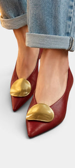 Mahaute Billini red pointed-toe pumps with a gold metallic ornament, worn with cuffed blue jeans.
