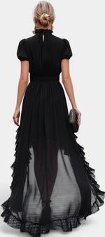 Back view of a woman wearing a Mahaute black asymmetrical long dress with ruffled hem and puffed sleeves