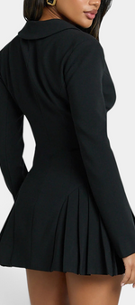 Model wearing a Mahaute black blazer dress with a cinched waist and pleated skirt, back view