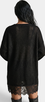 Back view of a model wearing a Mahaute black oversized knit sweater dress with a delicate floral lace hem.