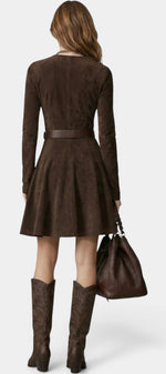 Back view of a woman wearing a Mahaute brown suede skater dress with a belted waist, long sleeves, and cowboy boots.