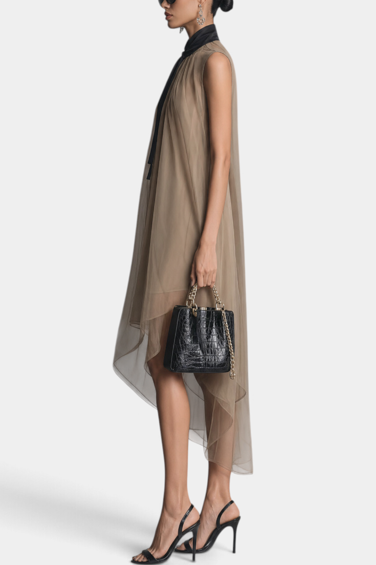 Model wearing a Mahaute Cecily asymmetrical midi dress in sheer beige voile with a black lavalliere collar and heels.