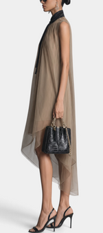 Model wearing a Mahaute Cecily asymmetrical midi dress in sheer beige voile with a black lavalliere collar and heels.