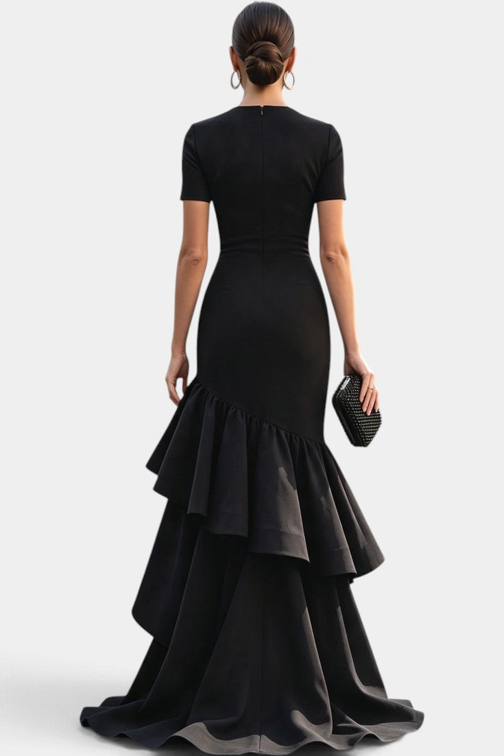 Back view of Mahaute Chantelle black floor-length gown with short sleeves, draped bodice, and asymmetrical ruffles.