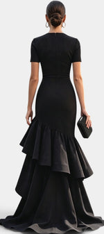 Back view of Mahaute Chantelle black floor-length gown with short sleeves, draped bodice, and asymmetrical ruffles.