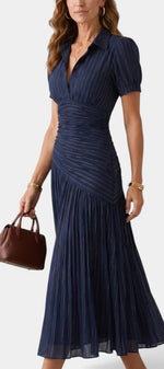 Robe mi-longue Dimitri de Mahaute à rayures bleues, plissée, avec col chemise et taille drapée, portée de profil.