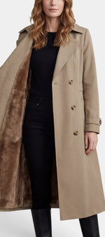 Mahaute Ermelinde trench long beige à doublure fourrure, ceinturé, avec double boutonnage, porté avec col relevé et poches latérales