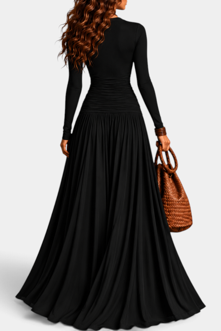 Mahaute Gracia long black dress with long sleeves, ruched waist, and flowing skirt, worn by a woman holding a bag.