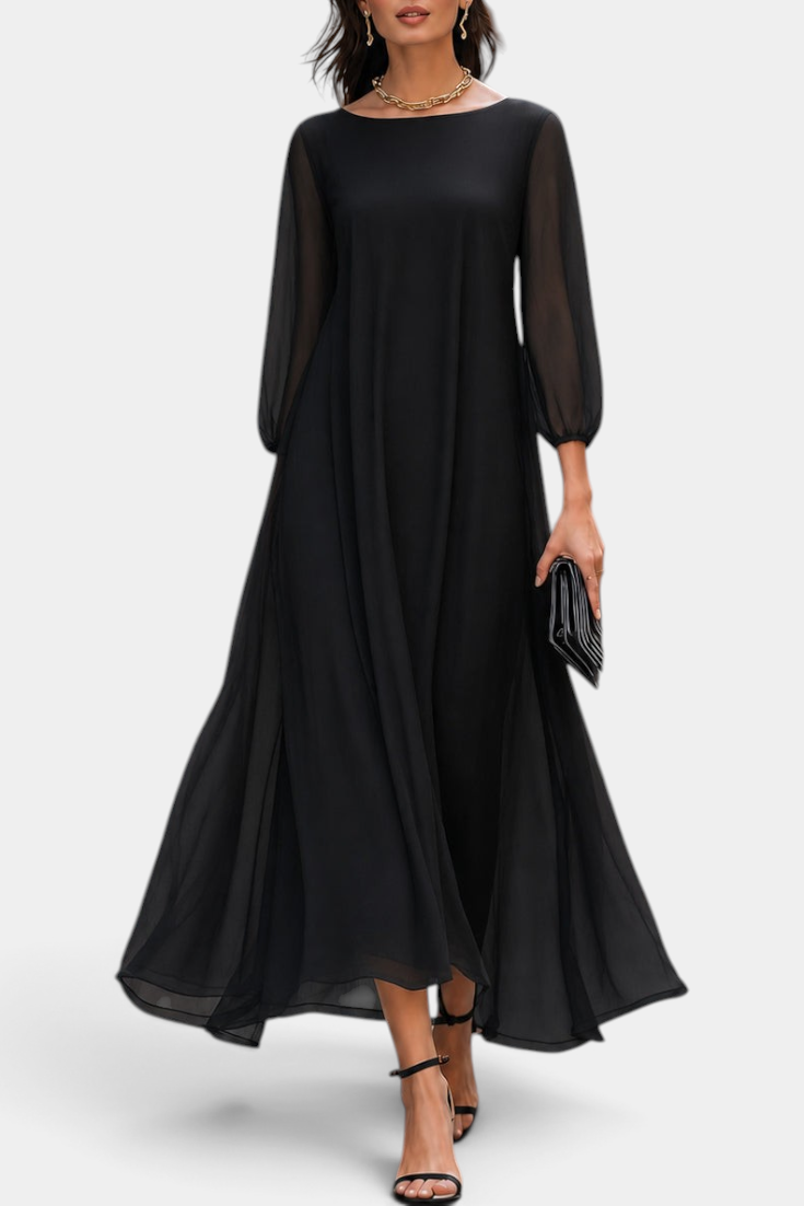 Mahaute Mazarine long black flowing dress with sheer sleeves and a flared skirt worn by a model on a city street