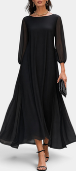 Mahaute Mazarine long black flowing dress with sheer sleeves and a flared skirt worn by a model on a city street