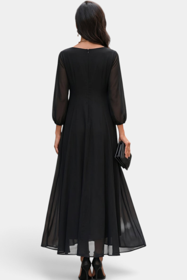 Back view of a woman wearing a Mahaute Mazarine black long flowing dress with sheer sleeves in a city street setting.