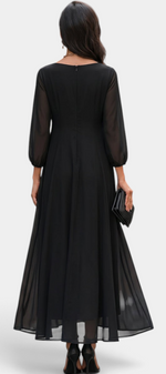 Back view of a woman wearing a Mahaute Mazarine black long flowing dress with sheer sleeves in a city street setting.