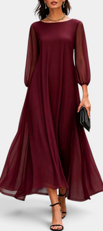 Mahaute Mazarine long burgundy flowing dress with sheer sleeves and flared skirt, worn with black heels on a city street.