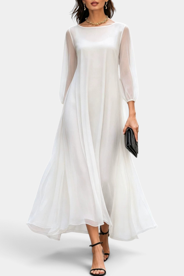 Mahaute Mazarine long white flowing dress with sheer sleeves and flared skirt, styled with black heels and a clutch.