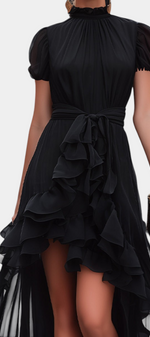 Mahaute Melusina black asymmetrical long dress with ruffled skirt, puffed sleeves, and a tied waist for evening wear.