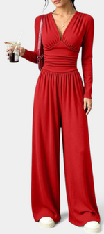 Mahaute Mirabel red long-sleeve jumpsuit with a V-neck, ruched bodice, cinched waist, and wide-leg trousers.