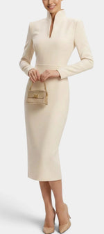 Mahaute Sandy cream midi dress with a high slit collar, long sleeves, and a fitted waist, styled with nude heels.