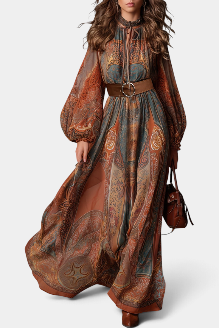 Mahaute Suevy long bohemian dress with ornamental print, tie neck, sheer puff sleeves, and a brown round-buckle belt.