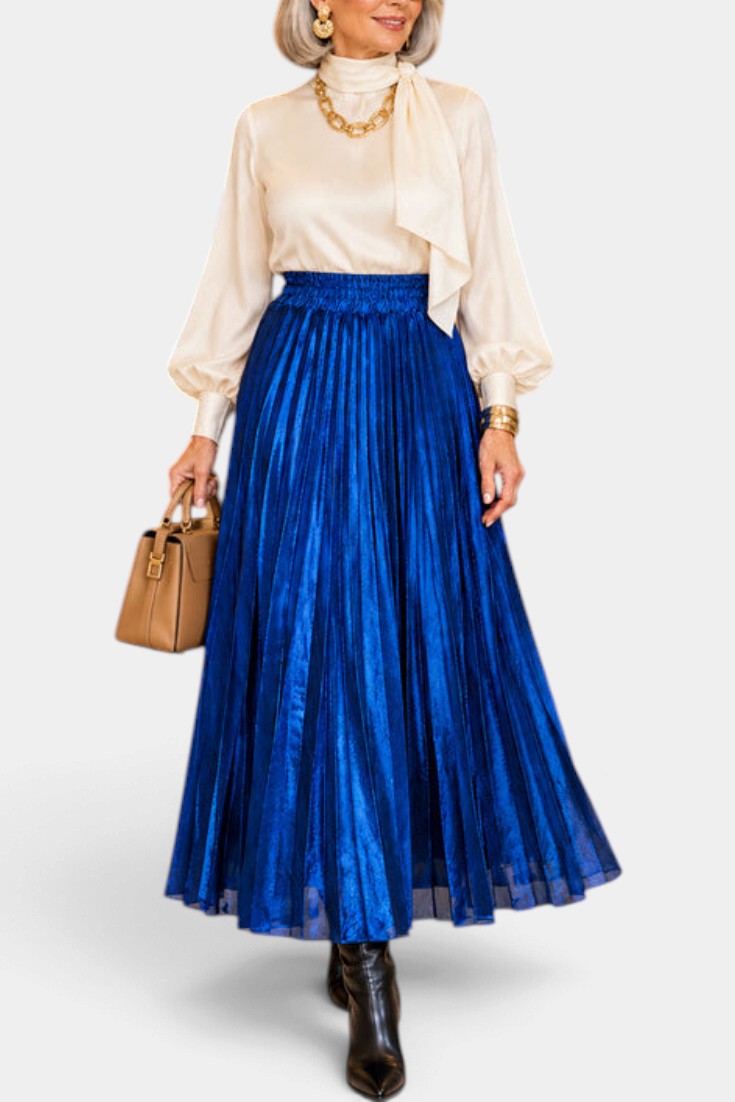 Mahaute Tegan high-waisted metallic blue pleated midi skirt worn with a cream blouse and brown handbag
