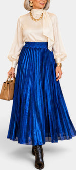 Mahaute Tegan high-waisted metallic blue pleated midi skirt worn with a cream blouse and brown handbag