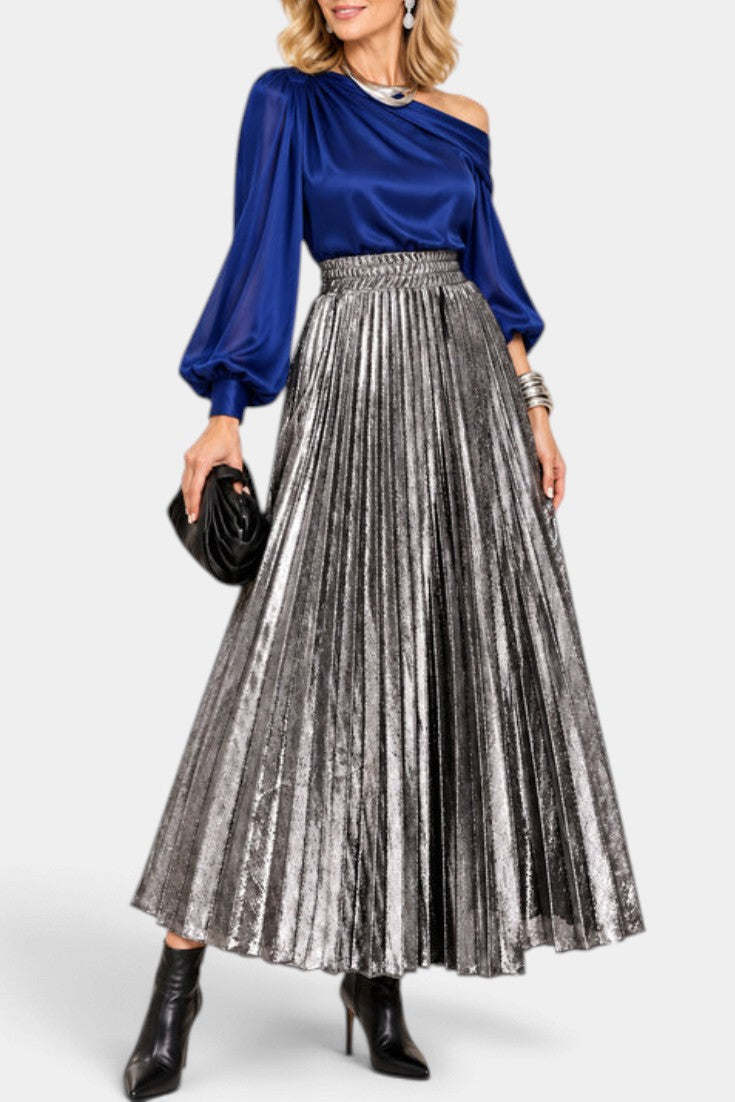 Mahaute Tegan high-waisted metallic pleated long skirt in silver, styled with a blue blouse and black ankle boots.