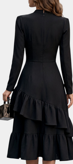 Mahaute Velislava black midi dress with long sleeves, cinched waist, and asymmetrical ruffled hem, back view.