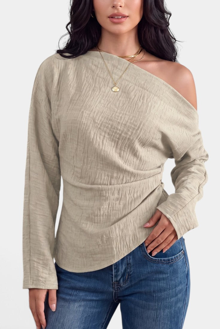 Top asymétrique beige Mahaute Zelmira avec épaule dénudée, manches longues et drapé à la taille, style élégant et moderne.