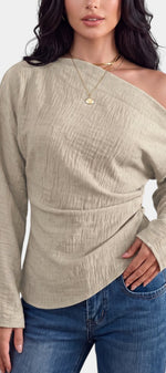 Top asymétrique beige Mahaute Zelmira avec épaule dénudée, manches longues et drapé à la taille, style élégant et moderne.
