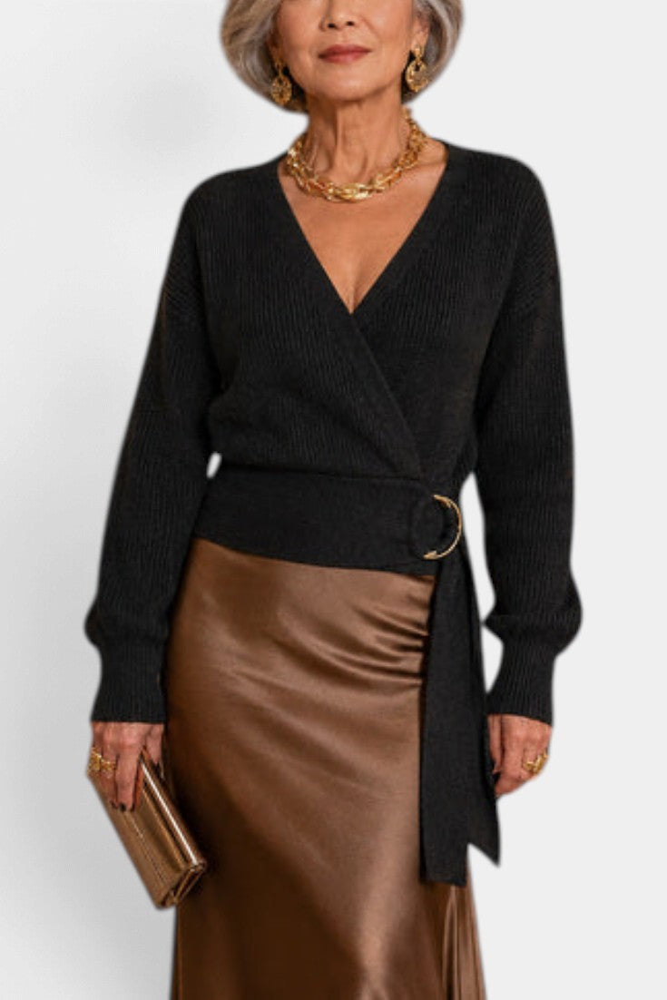 Mahaute Zia black knit wrap sweater with V-neck, long sleeves, and a gold-ring tie belt worn with a satin skirt.