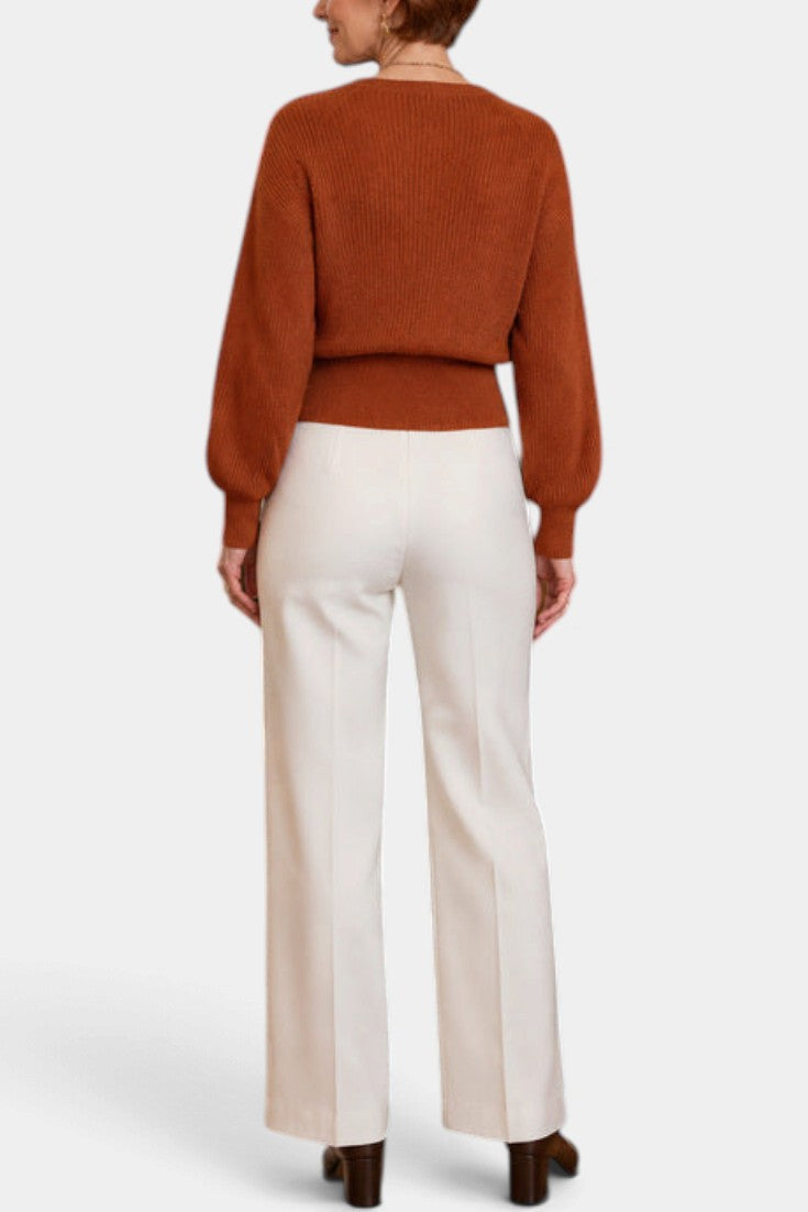 Mahaute Zia rust orange knit wrap sweater with long puff sleeves paired with white high-waisted trousers, back view