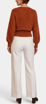 Mahaute Zia rust orange knit wrap sweater with long puff sleeves paired with white high-waisted trousers, back view